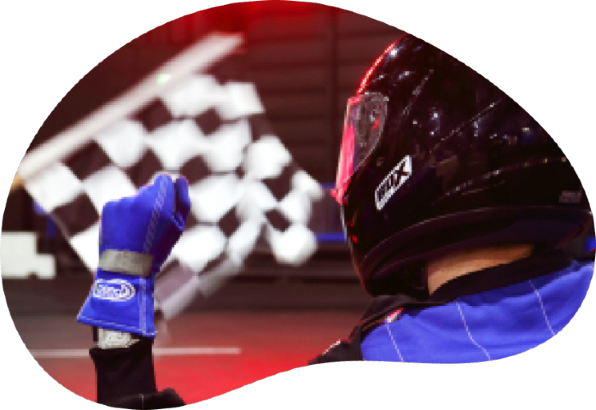 Person wearing a race suit & helmet in a go kart at the race track at Rogue Leisure with a chequered flag in the background