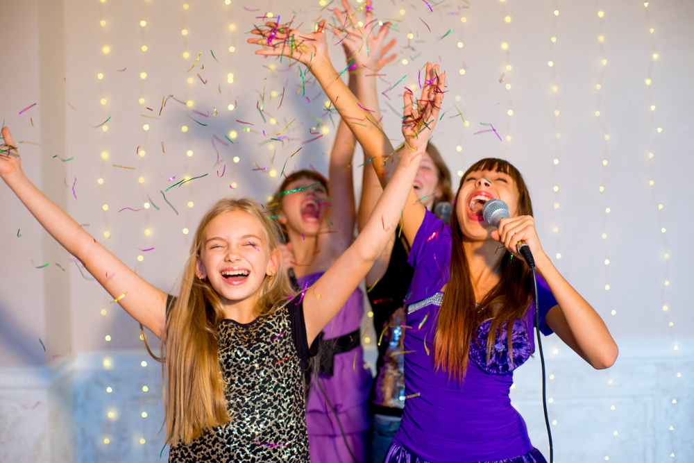 teenage girls with their hands up dancing and singing karaoke. Smiling and having fun.